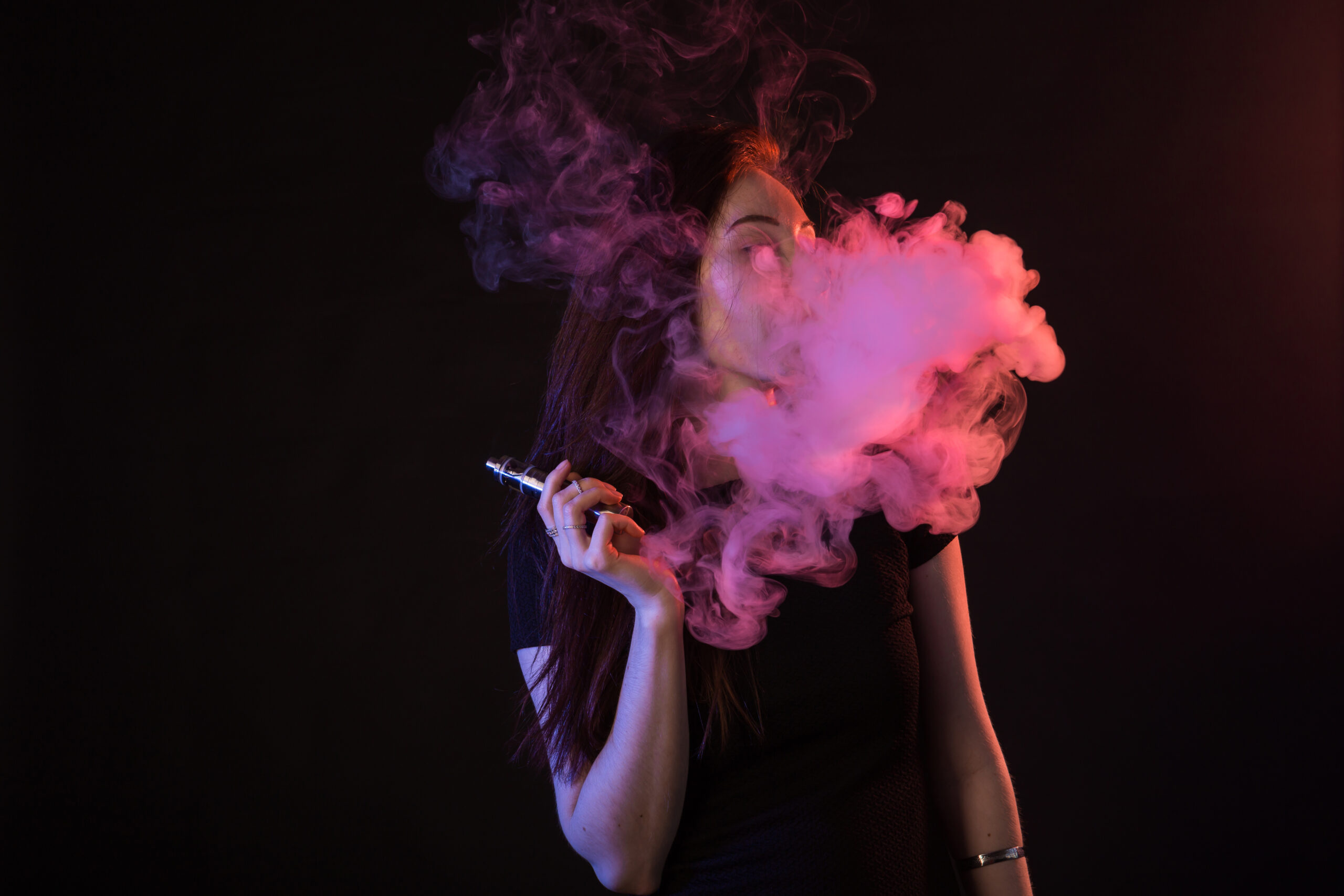 Young woman in neon light and smoke of e-cigarettes or vape on black background